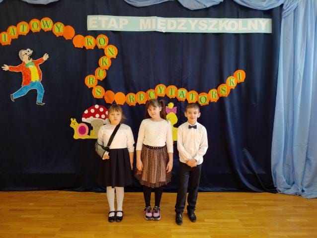 Troje uczniów na tle dekoracji konkursu recytatorskiego. 