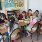 Poczęstunek - uczniowie klasy siedzą przy stoliczkach i jedzą słodkości.